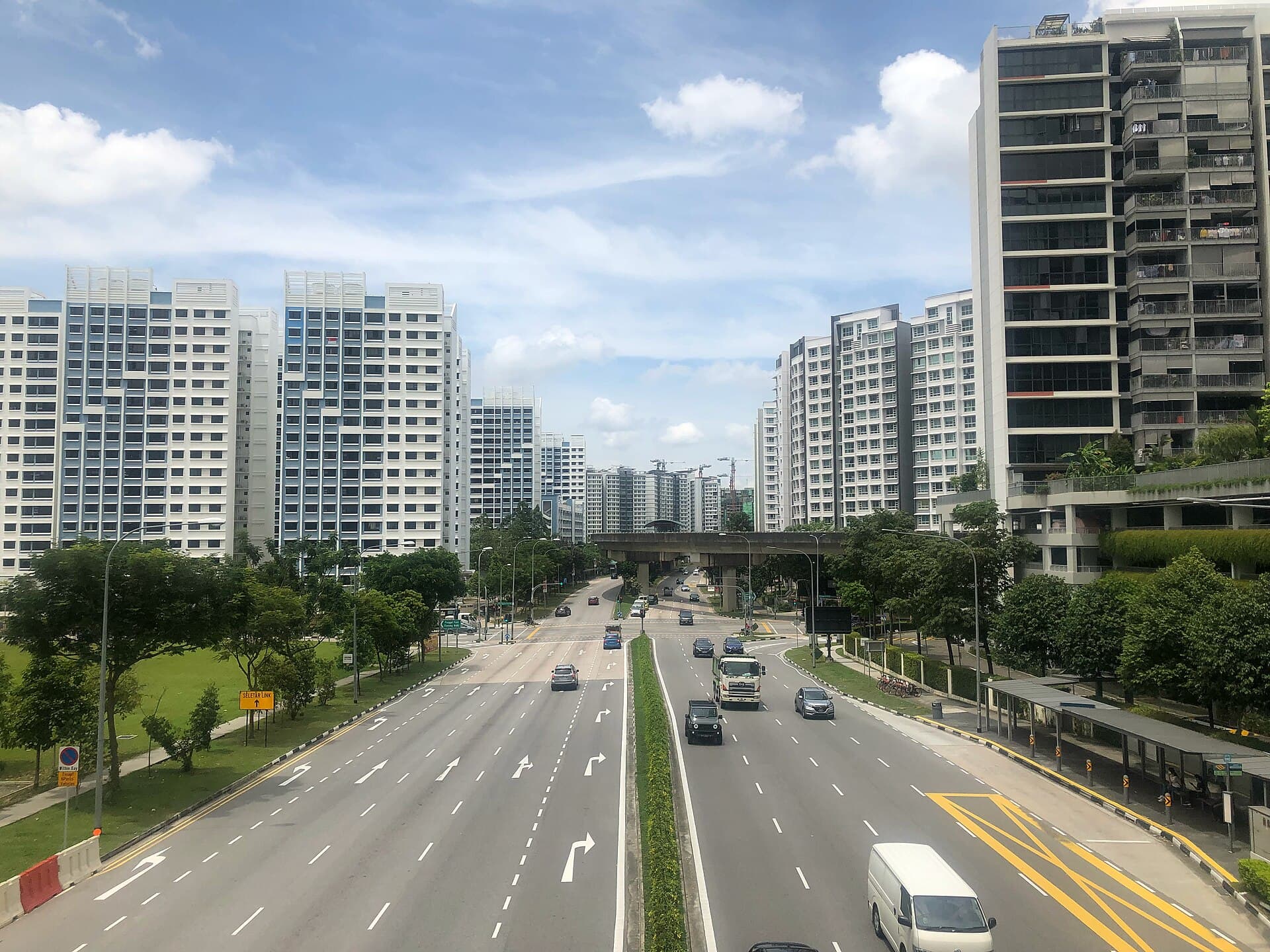 View from a pedestrian bridge looking north along Punggol Way, with new high-rise flats and the wide roads of a waterway town
